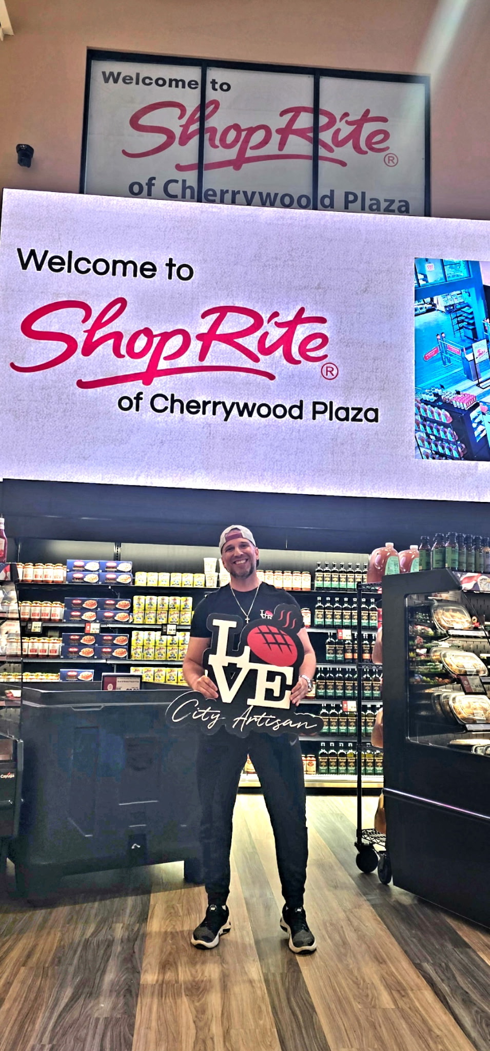 Love City Artisan owner holding a branded sign inside ShopRite of Cherrywood Plaza